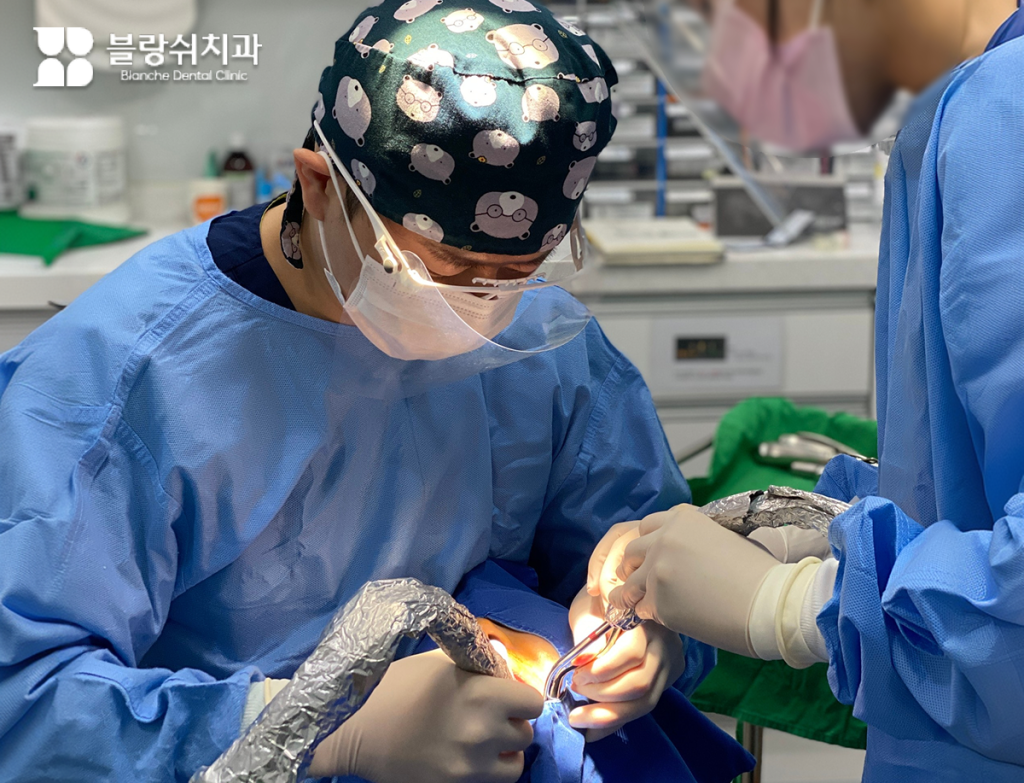 멸균된 수술복을 착용한 블랑쉬치과 의료진이 수면 치료 치과 시스템을 활용하여 환자의 임플란트 수술에 집중하고 있는 전문적인 현장